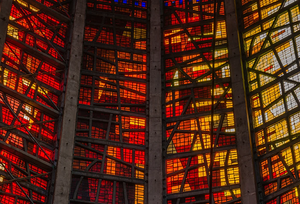 Tall stained-glass panels in vivid red, orange and yellow, divided by vertical concrete ribs and dark lead lines into a geometric grid of rectangles and diagonal shapes.