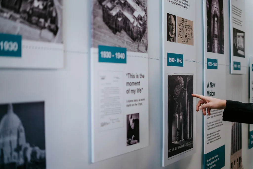 A hand pointing at a 1940–1950 panel on a museum timeline display featuring a black-and-white photograph and accompanying text, with adjacent timeline panels visible.